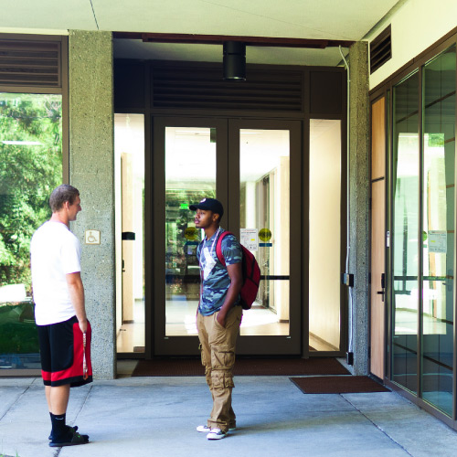 Two students conversing in front of the Language Arts and Social Science building